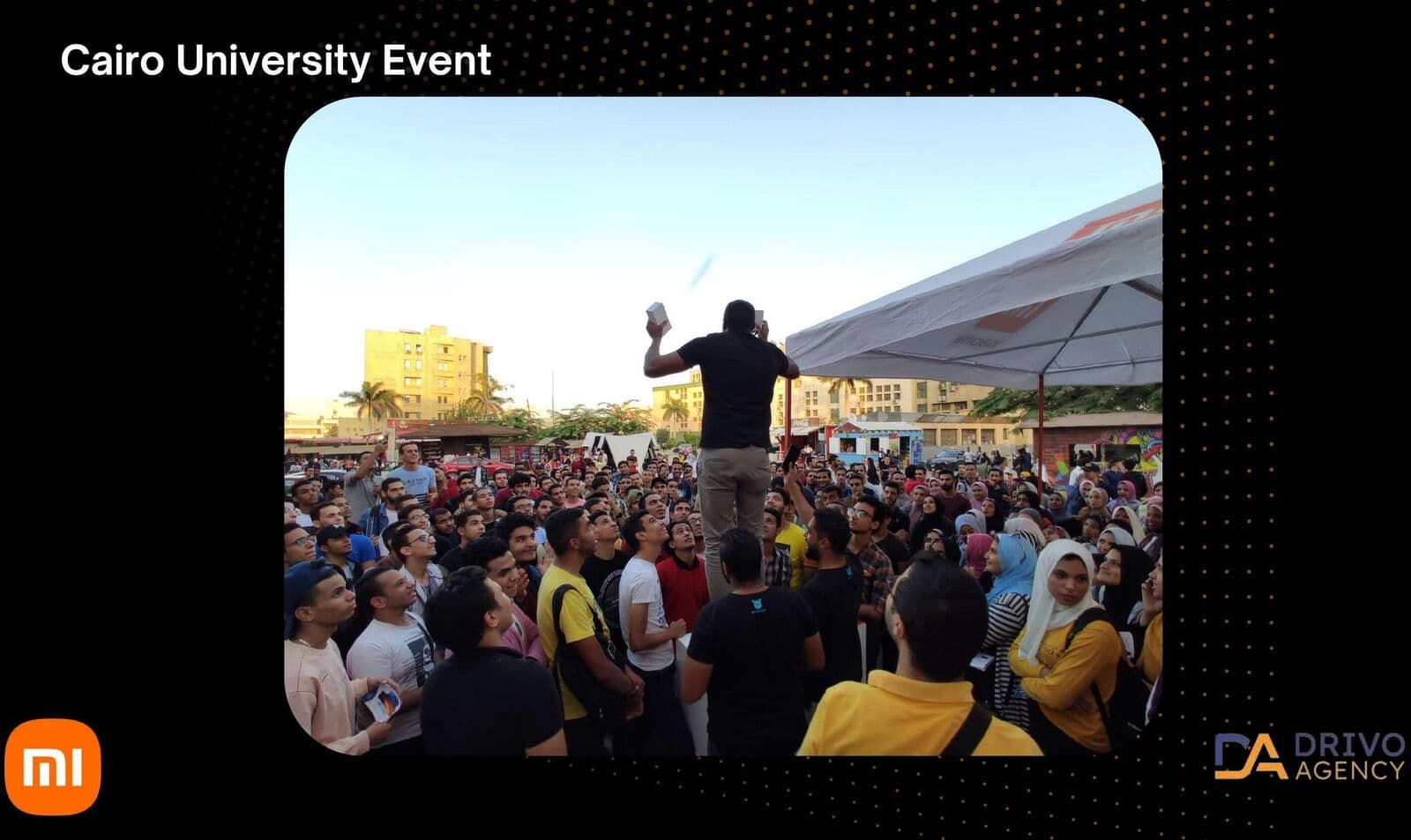 A presenter addressing a dense student crowd at Cairo University at dusk