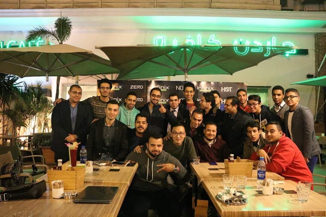 A group of about 20 people at an outdoor café at night, in front of a step-and-repeat backdrop reading Infinix Zero, Infinix NOTE, and Infinix HOT