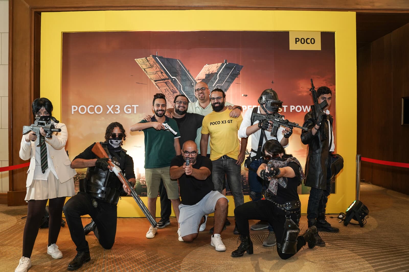 A group of attendees in costume posed in front of a branded 'POCO X3 GT' photo backdrop