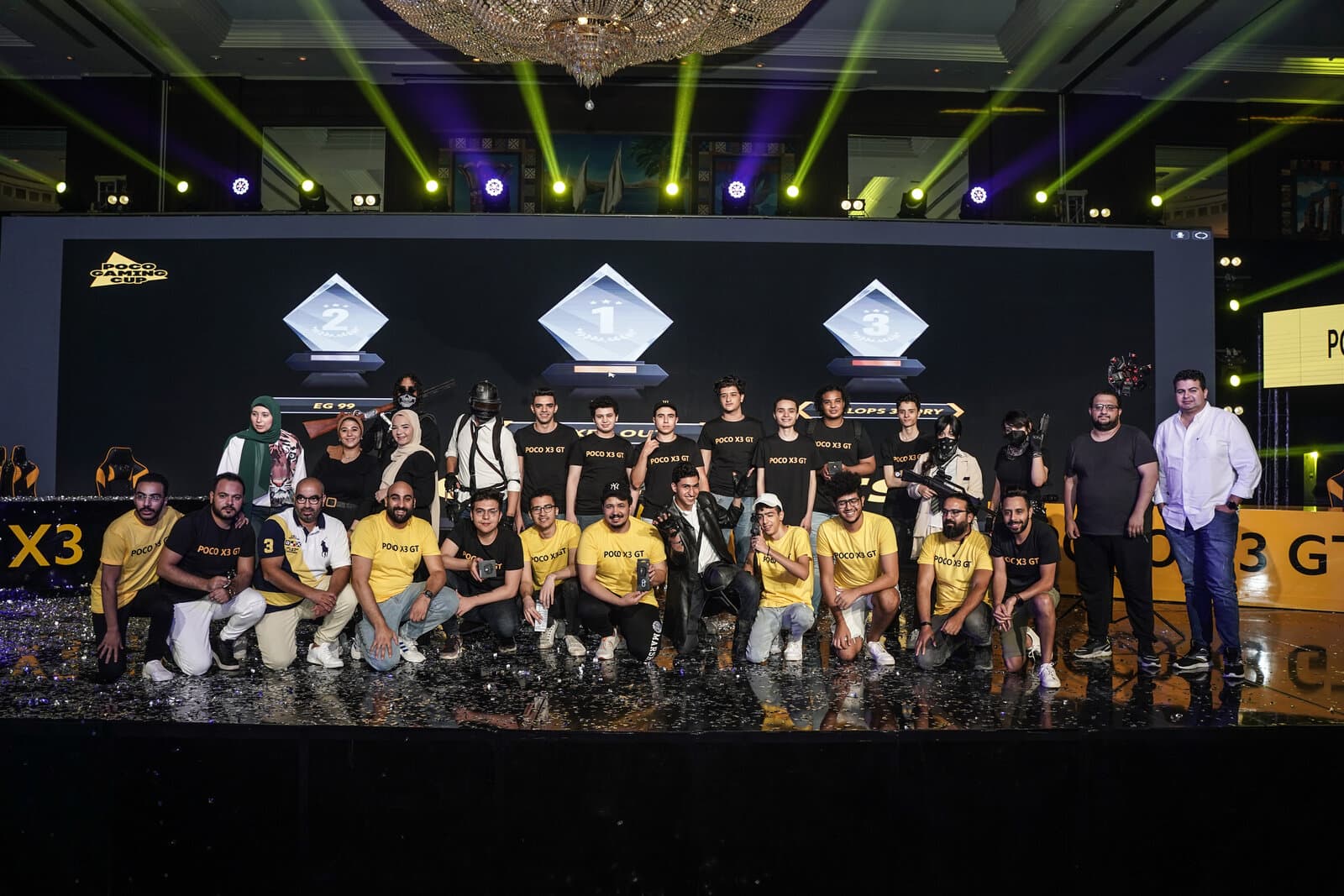 The top three POCO Gaming Cup teams on stage with 1st/2nd/3rd place trophies displayed behind them
