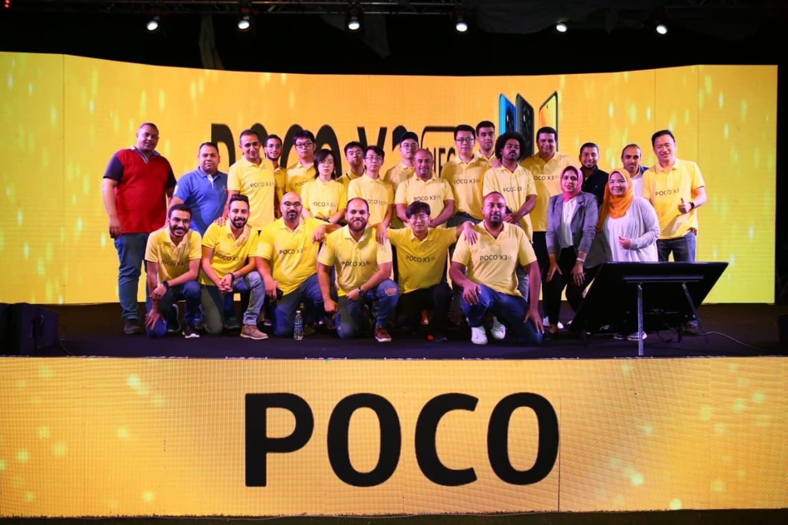 The same team on stage at the POCO X3 NFC launch event, large 'POCO' branding on the backdrop and stage front
